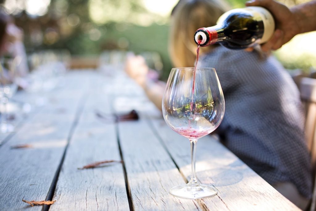 An image of wine being poured into a glass on a picnic table