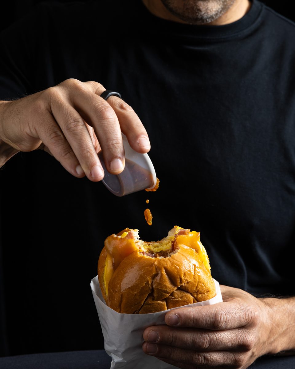 Chef Dan Figone adding signature hot sauce to a Handheld Catering brioche burger