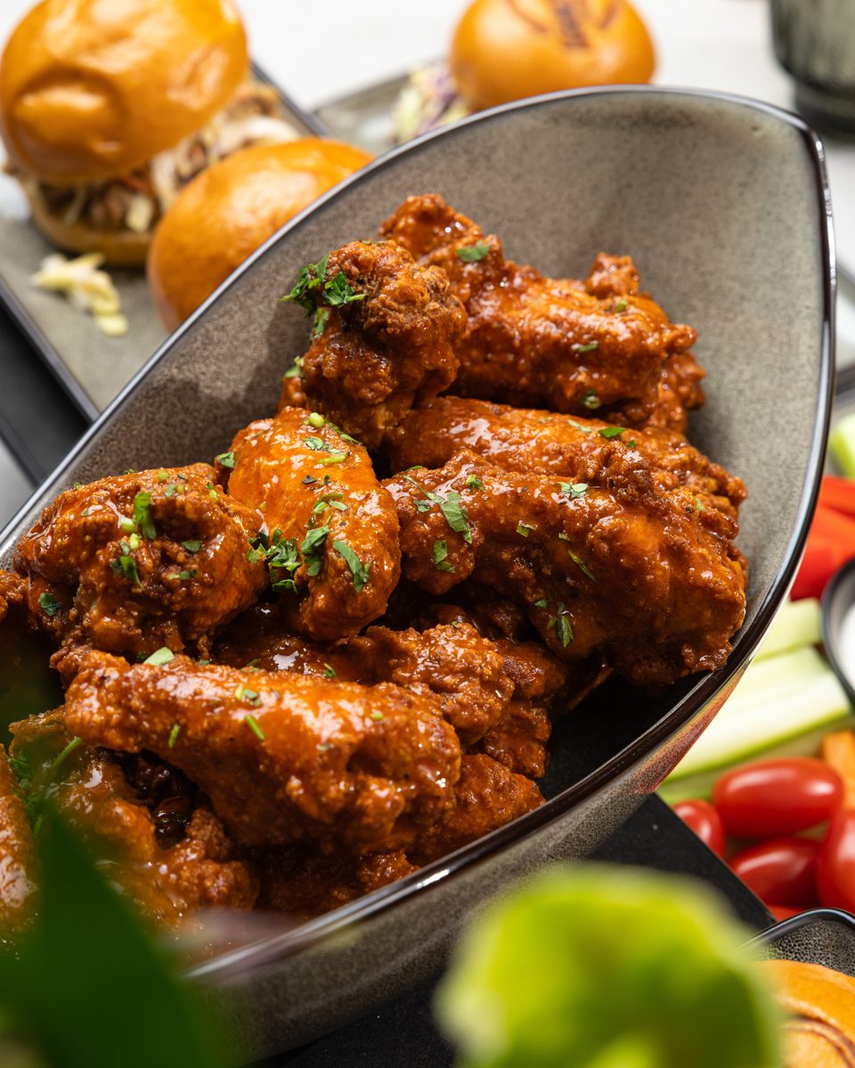 Glazed buffalo chicken wings with fresh herbs served at a small gathering by Handheld Catering