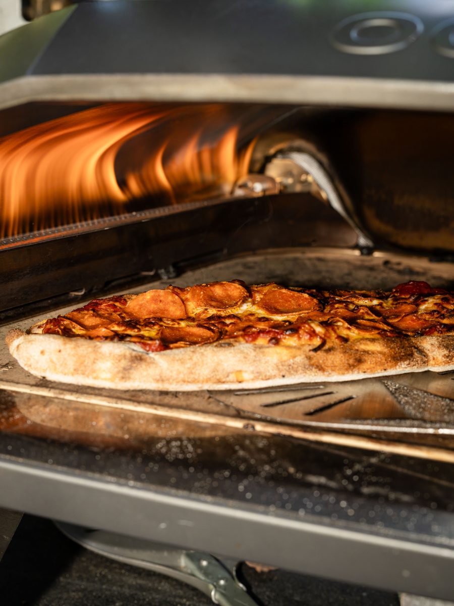 A made-to-order pizza baking inside Handheld Catering's wood-fired oven at a private Los Altos backyard graduation party