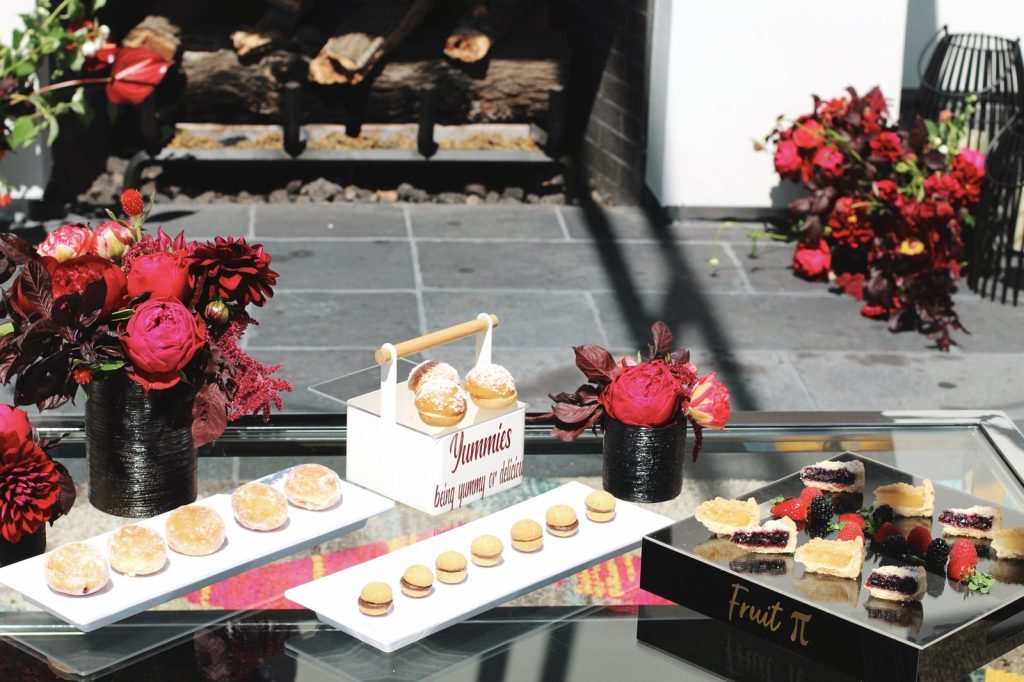 Handheld Catering summer dessert station with mini pastries, fruit tarts, and rich red floral arrangements for a Bay Area event